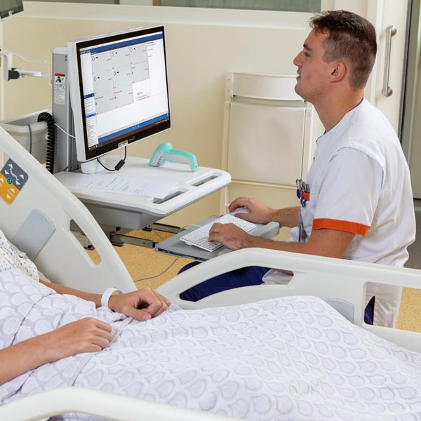 Hospital nurse using a MediPod Power workstation next to a patient in bed